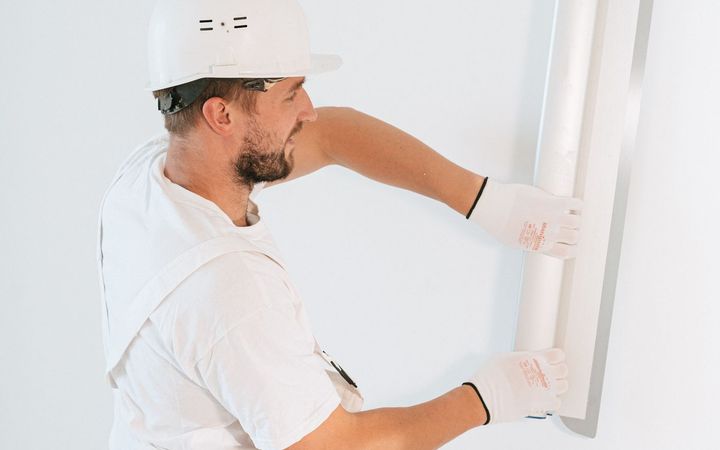 Worker in a hard hat fitting a sheet of drywall against a wall