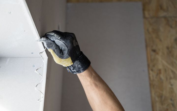 Gloved hand spreading joint compound along a drywall corner