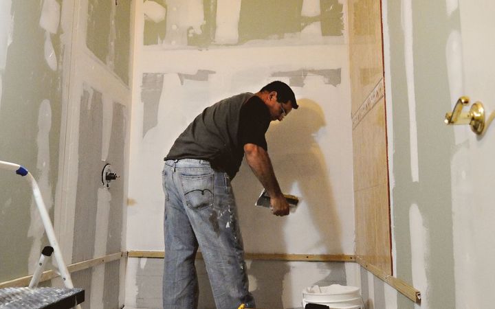 Man finishing drywall joints on green moisture-resistant board in a bathroom