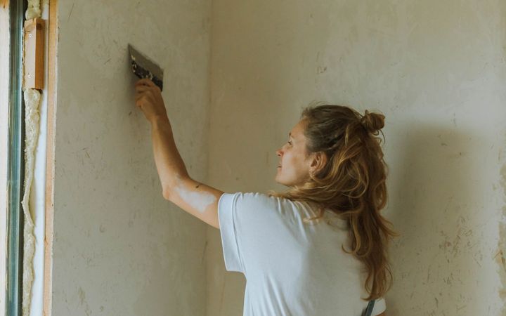Woman skim-coating an old wall with a trowel
